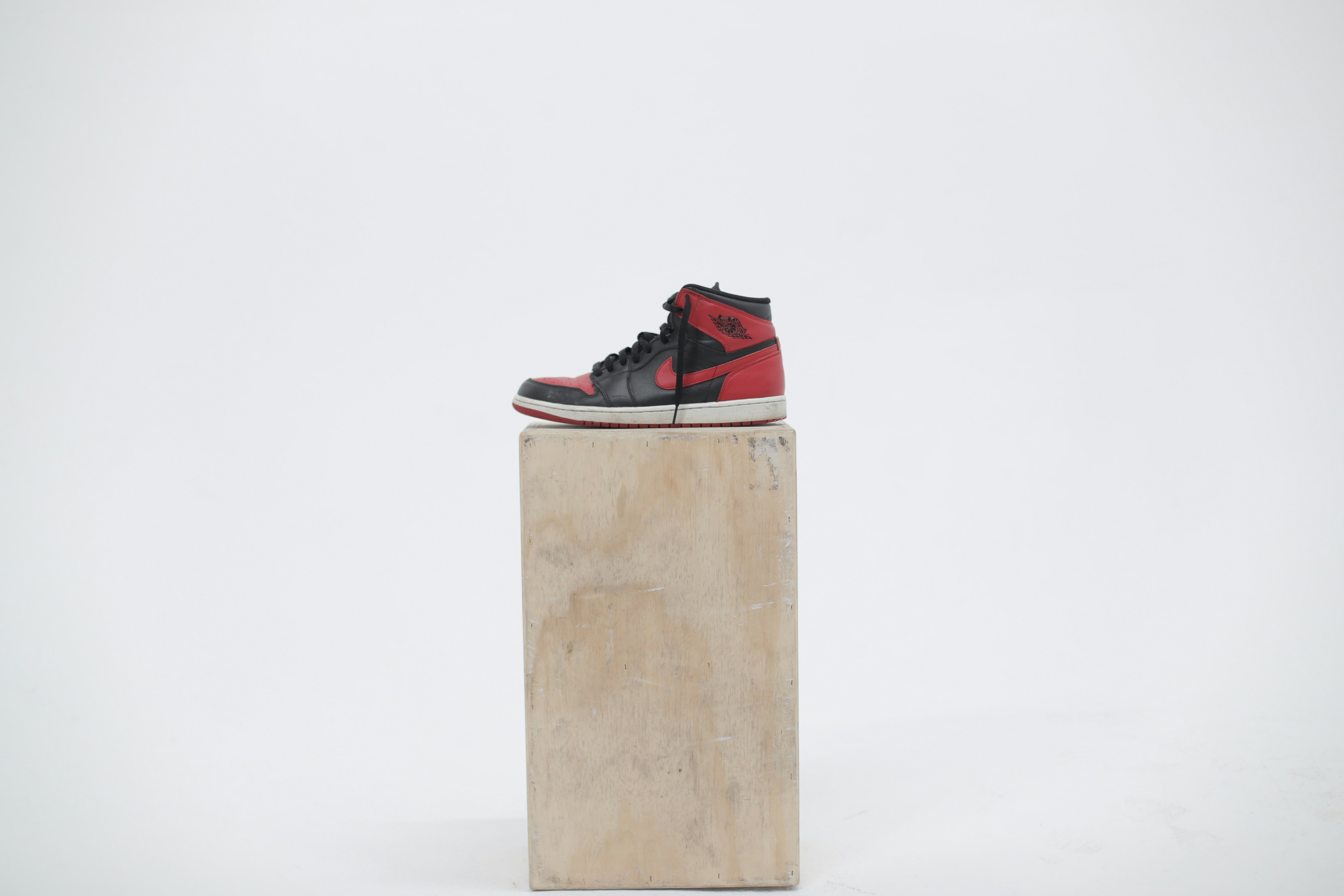 unpaired black and red Air Jordan 1 shoe on wooden box